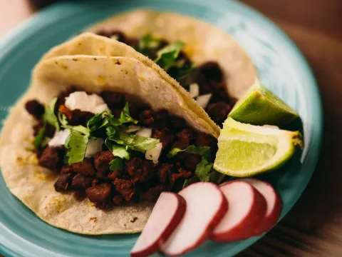 Two chorizo street tacos on soft corn tortillas topped with cilantro and onion, with lime wedges and sliced radish on a turquoise plate, at Boca Chica in Saint Paul