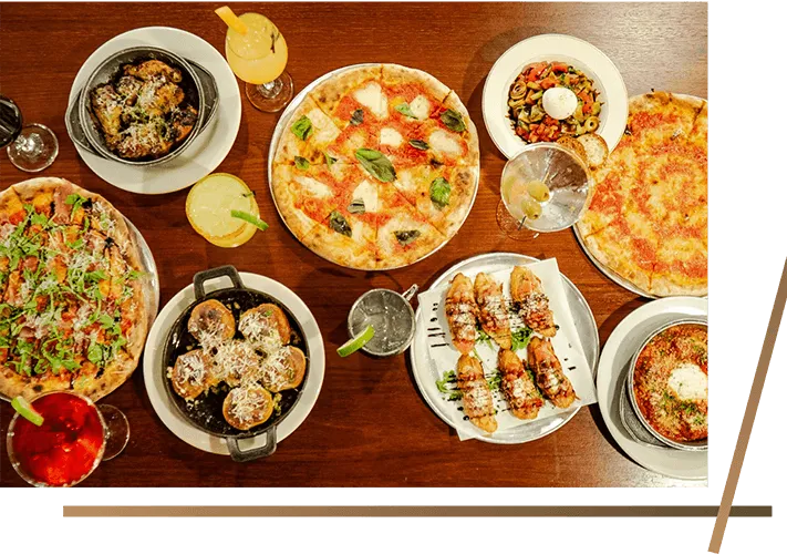 Pizzas, salad and small plates spread across a wooden table at La Pizzeria Metro