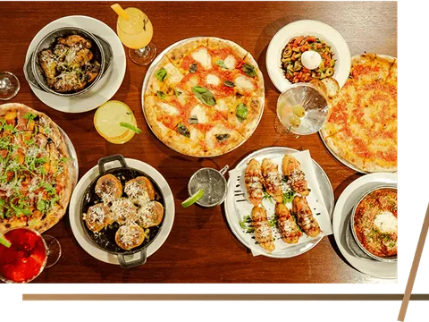 Pizzas, salad and small plates spread across a wooden table at La Pizzeria Metro