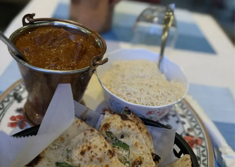 A rich tandoori-style curry served in a copper bucket with garlic naan and basmati rice on a set table at Rangoli India Restaurant, San Jose