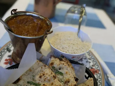 A rich tandoori-style curry served in a copper bucket with garlic naan and basmati rice on a set table at Rangoli India Restaurant, San Jose