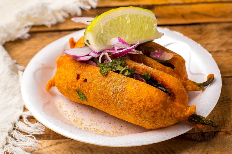 Mirchi bajji, a batter-fried chilli fritter topped with sliced red onion and a lime wedge on a plate, at Bawarchi Biryanis in Sandy Springs, Georgia