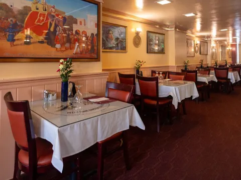 Dining room with white-clothed tables and framed Indian artwork at India Quality Restaurant