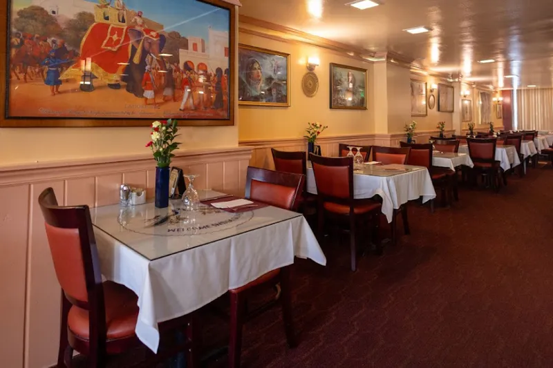 Dining room with white-clothed tables and framed Indian artwork at India Quality Restaurant