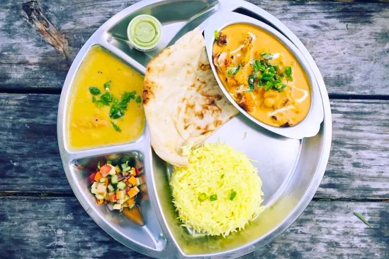 A Zareen's thali with chicken tikka masala, tarka daal, chopped salad and green chutney, naan and saffron rice on a steel platter