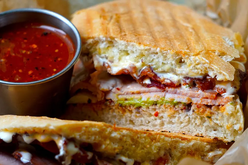 A wood-oven torta sliced open, served with a cup of red salsa at Xoco