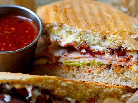 A wood-oven torta sliced open, served with a cup of red salsa at Xoco
