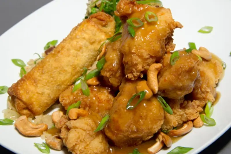 A plate of Leong's Springfield-style cashew chicken — battered fried chicken in brown oyster gravy with cashews and scallions, served with fried rice and an egg roll