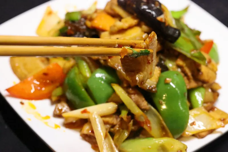 Home-style twice-cooked pork stir-fried with green peppers, red pepper and scallions on a white plate at Najia Cafe