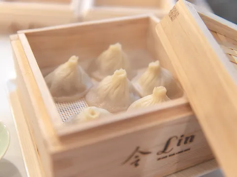 A bamboo steamer of xiao long bao soup dumplings branded with the restaurant's own '令 Lin' logo and 'Asian Bar + Dim Sum' mark, served at Lin Asian Bar + Dim Sum at 1203 W 6th Street in Austin