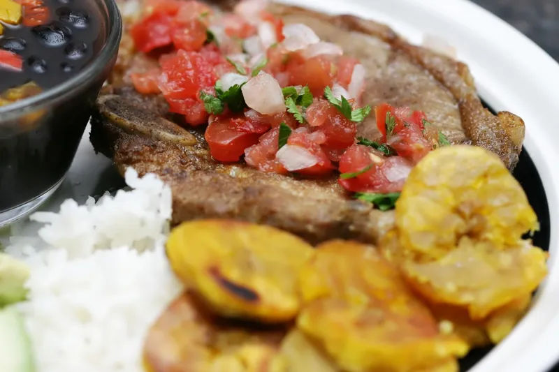 A Cuban plate of palomilla steak topped with tomato and onion, white rice, tostones and black beans at Rincon Criollo in Miami.