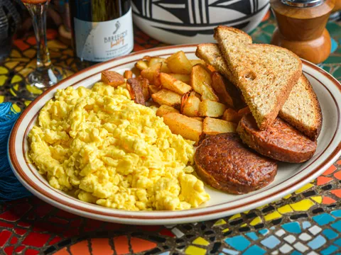 Breakfast plate with scrambled eggs, home-fried potatoes, grilled chorizo sausage and wheat toast on a colorful mosaic-tiled table at Church Street Cafe in Old Town Albuquerque