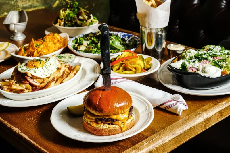 Spread of Au Cheval dishes including the griddled double cheeseburger, loaded fries with a fried egg, hash browns, chopped salad and pickles