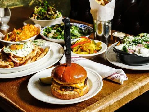 Spread of Au Cheval dishes including the griddled double cheeseburger, loaded fries with a fried egg, hash browns, chopped salad and pickles