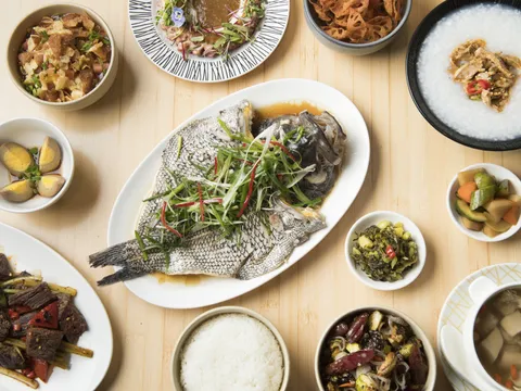 Overhead spread of Pinch Chinese dishes including whole steamed fish with scallions, cumin beef, congee, braised eggs and rice