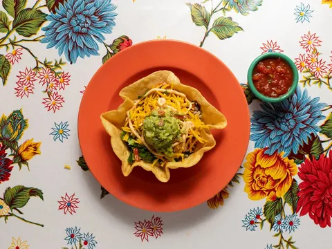 Taco salad in a tortilla bowl with guacamole and cheese beside a dish of salsa at Elote Cafe