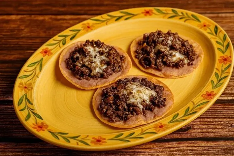 Three crispy corn tostadas topped with seasoned ground beef and melted cheese on a hand-painted talavera plate at Los Carboncitos in Denver