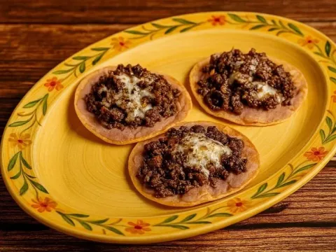 Three crispy corn tostadas topped with seasoned ground beef and melted cheese on a hand-painted talavera plate at Los Carboncitos in Denver