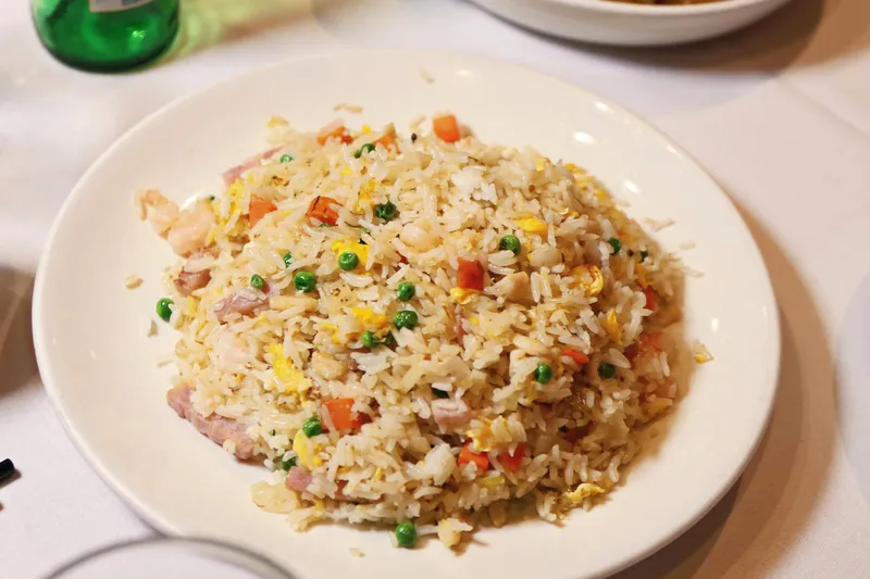 House special fried rice with shrimp, roast pork and green peas on a white plate at Dim Sum Go Go, a plate of chow fun and a Tsingtao beer behind