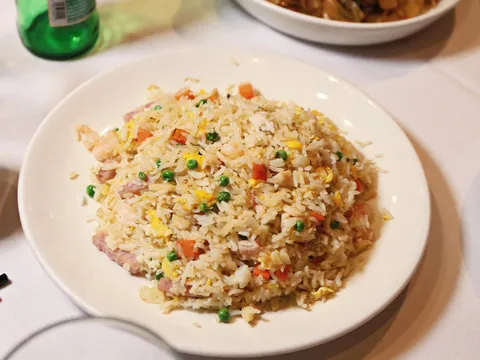 House special fried rice with shrimp, roast pork and green peas on a white plate at Dim Sum Go Go, a plate of chow fun and a Tsingtao beer behind