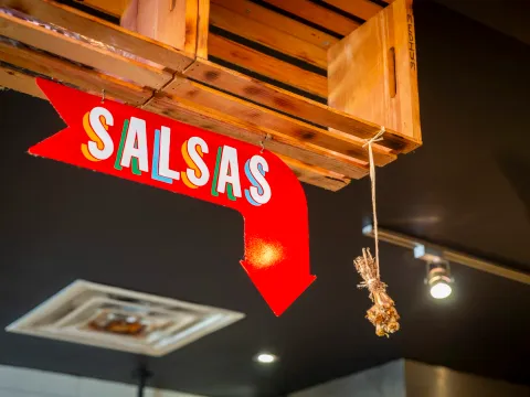 Interior detail at Resident Taqueria in Dallas: a red hand-painted 'Salsas' arrow sign hanging beneath a wooden crate shelf, with a bundle of dried chiles alongside