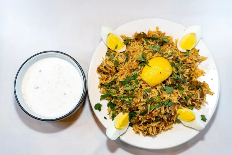 Plate of biryani with boiled egg and a bowl of raita at Mirch Masala