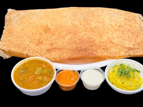 A crispy golden masala dosa served with sambar, tomato and coconut chutneys and potato masala in takeout cups at Saffron Cafe in Norcross.
