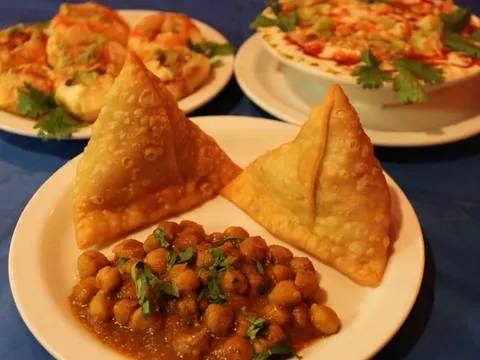 Plate of two samosas with a bowl of chole (spiced chickpeas) alongside dahi puri and papri chaat at India Chaat Cafe in Dallas