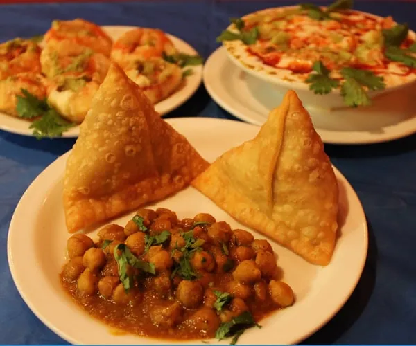 Plate of two samosas with a bowl of chole (spiced chickpeas) alongside dahi puri and papri chaat at India Chaat Cafe in Dallas
