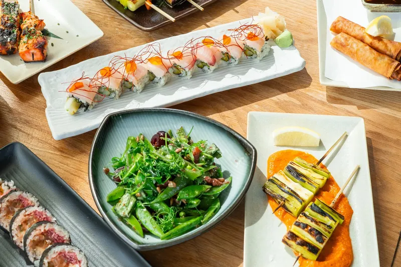 Table spread at AFURI Izakaya in Portland with a sushi roll, charcoal-grilled skewers, a snap pea salad, and crispy spring rolls