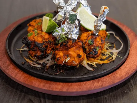 Sizzling tandoori chicken tikka with foil-wrapped drumsticks and lime on a cast-iron platter at Tap N Tikka in Gilbert.