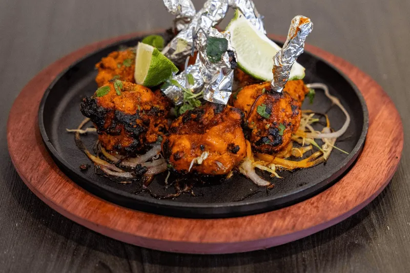 Sizzling tandoori chicken tikka with foil-wrapped drumsticks and lime on a cast-iron platter at Tap N Tikka in Gilbert.