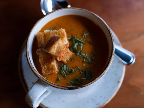 Duckfat's cream of tomato fennel soup topped with grilled cheese croutons and herbs, served in a rustic mug at Duckfat in Portland