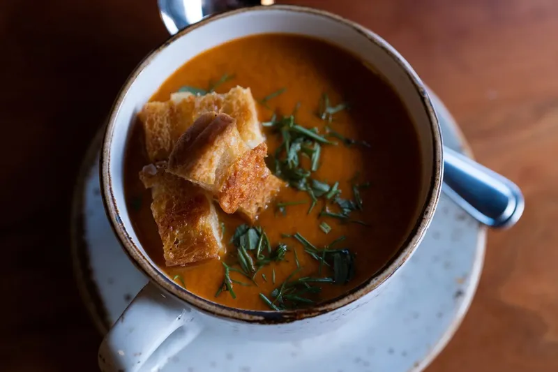Duckfat's cream of tomato fennel soup topped with grilled cheese croutons and herbs, served in a rustic mug at Duckfat in Portland