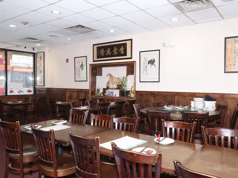 Wood-paneled dining room at Dumpling Cafe in Boston Chinatown with round and square tables, Chinese calligraphy wall art, and a window looking onto Washington Street