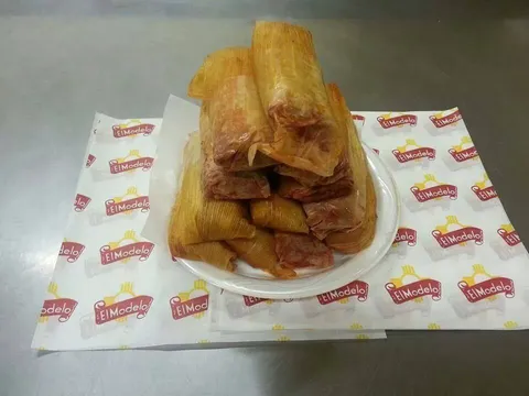 A plate of large handmade pork tamales in corn husks stacked on El Modelo branded paper at El Modelo Mexican Foods in Albuquerque