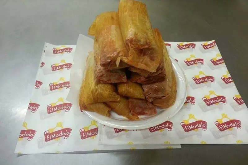A plate of large handmade pork tamales in corn husks stacked on El Modelo branded paper at El Modelo Mexican Foods in Albuquerque