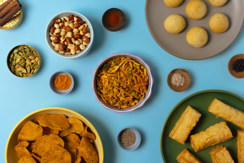Assortment of Gujarati snacks and farsan at Jay Bharat — sev mixture, dhokla, savory chips, and puff pastry, with bowls of spices