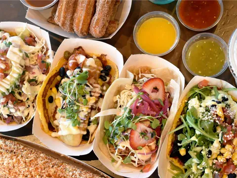 Four gourmet City Tacos in paper boats topped with microgreens, strawberry, arugula and cotija, alongside churros, salsas and elote