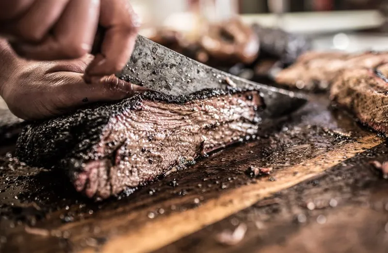 Hand slicing smoked brisket on a cutting board at Pecan Lodge