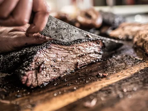 Hand slicing smoked brisket on a cutting board at Pecan Lodge