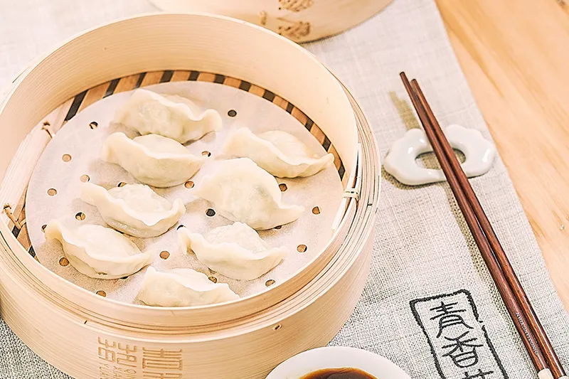 Steamed Qing Xiang Yuan dumplings in a bamboo steamer with dipping sauce and the restaurant's branded linen