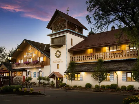 Dusk exterior of the Frankenmuth Bavarian Inn Restaurant, a Bavarian-style building with a clock tower, glockenspiel, flower boxes and a "World Famous Chicken Dinners" sign