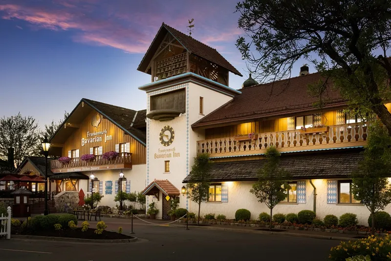 Dusk exterior of the Frankenmuth Bavarian Inn Restaurant, a Bavarian-style building with a clock tower, glockenspiel, flower boxes and a "World Famous Chicken Dinners" sign