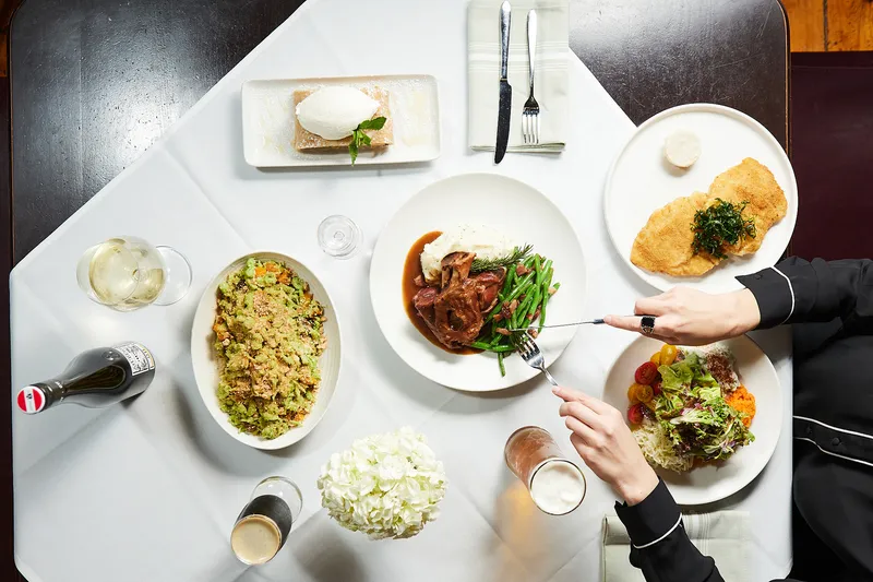 Overhead spread of Wiener schnitzel, braised lamb shank with mashed potatoes and green beans, apple strudel, and salads at Grünauer in Kansas City.