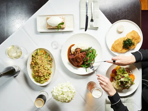 Overhead spread of Wiener schnitzel, braised lamb shank with mashed potatoes and green beans, apple strudel, and salads at Grünauer in Kansas City.