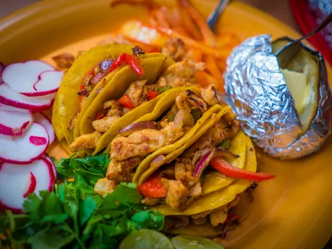 Plate of chicken fajita tacos on corn tortillas with sliced radishes, cilantro and a foil-wrapped baked potato at Tacos Chinampa in El Paso