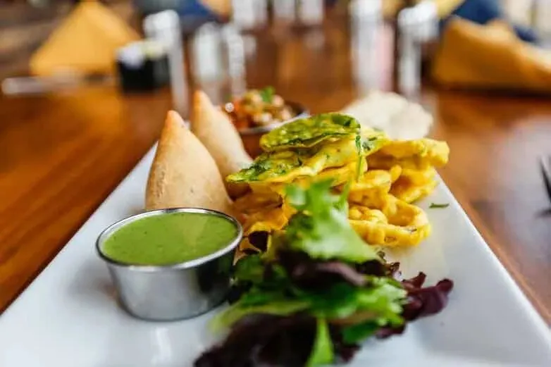 Assorted Indian appetizers with samosas, fritters, chutney, and greens at Saffron Valley Sugar House