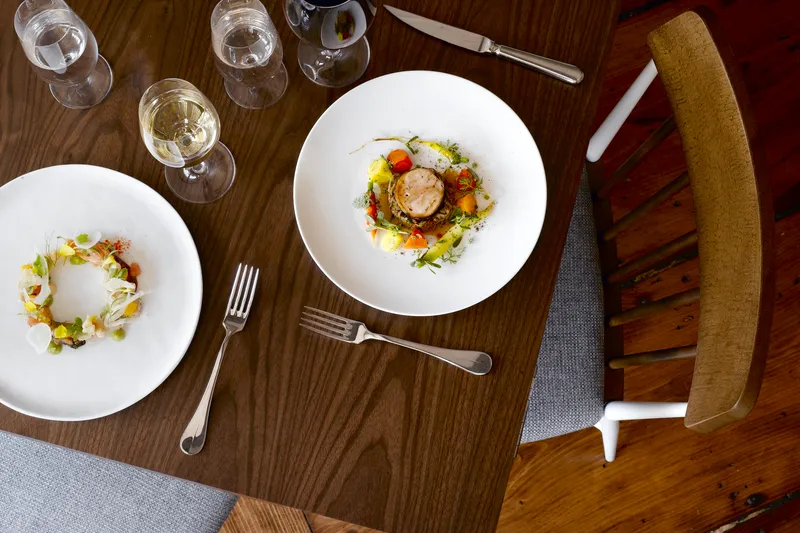 Two plated seasonal dishes with wine glasses on a walnut table at Persimmon in Providence