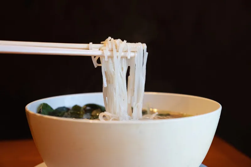 Chopsticks lifting rice noodles from a steaming bowl of pho at Mai Lee in Brentwood, Missouri